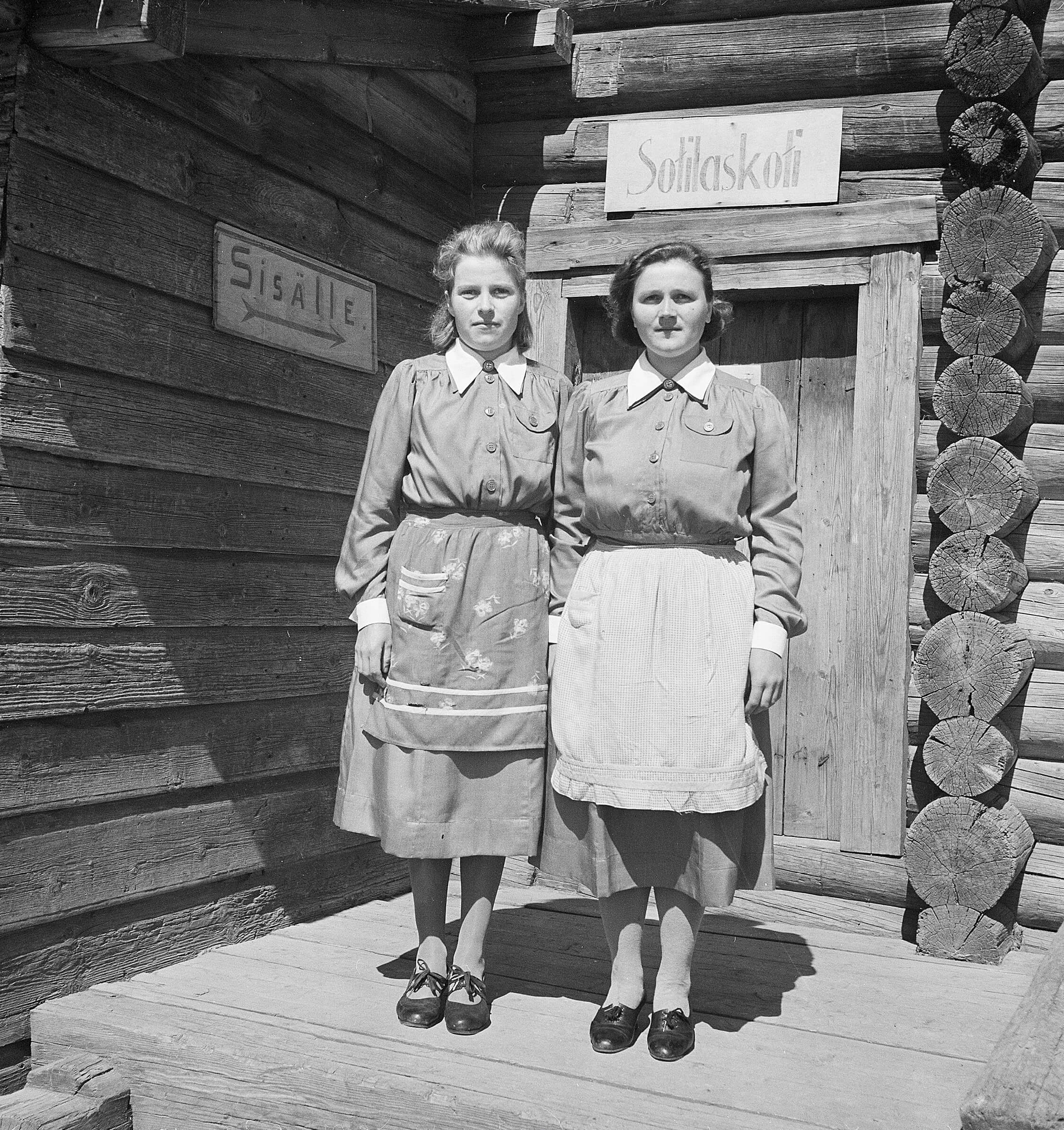 Kaksi sotilaskotisisarta sota-aikana seisomassa sotilaskodin edessä.